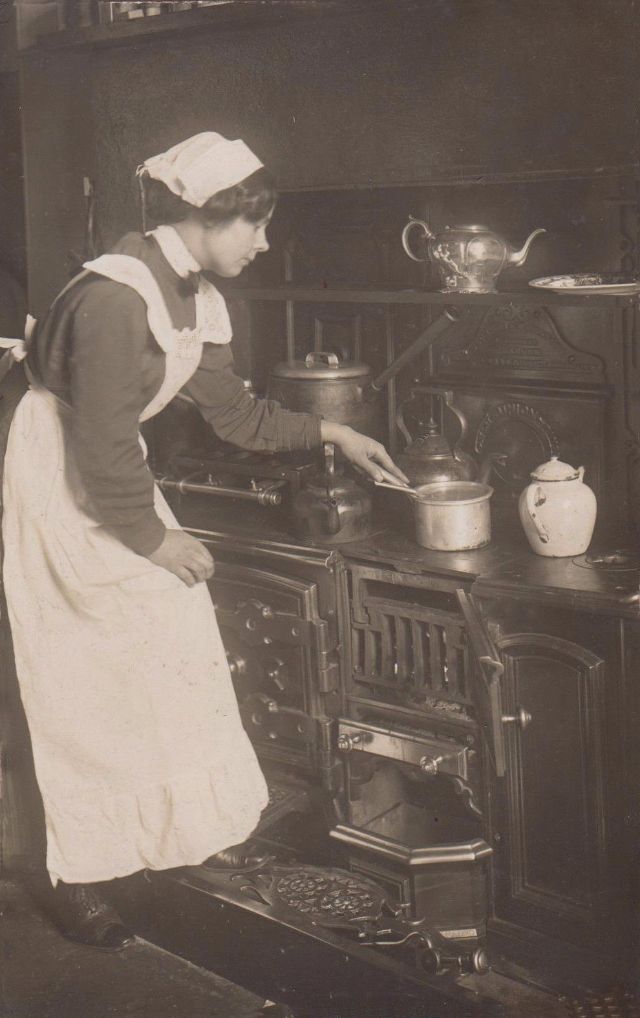Victorian Maid tending to pots on an old fashioned cast iron cooker.